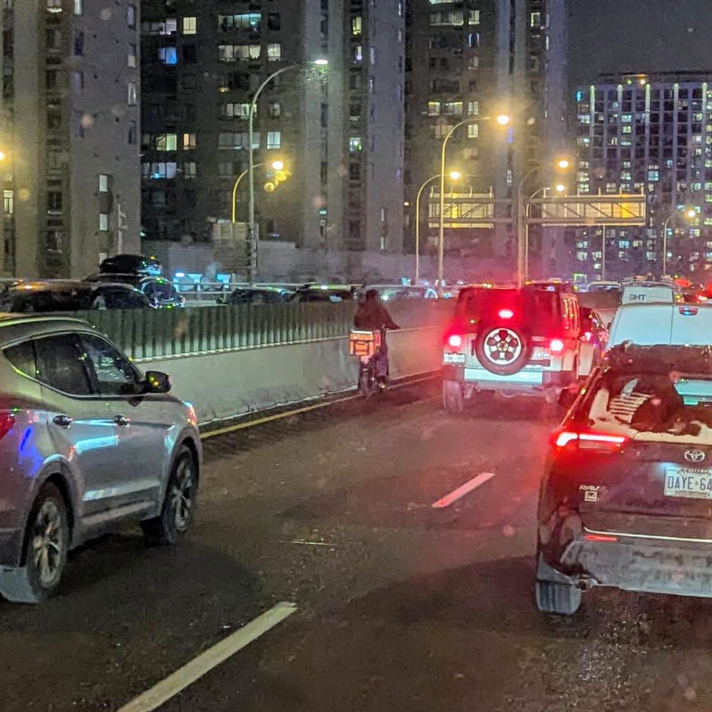 A cyclist riding a delivery ebike on the QEW highway among car traffic