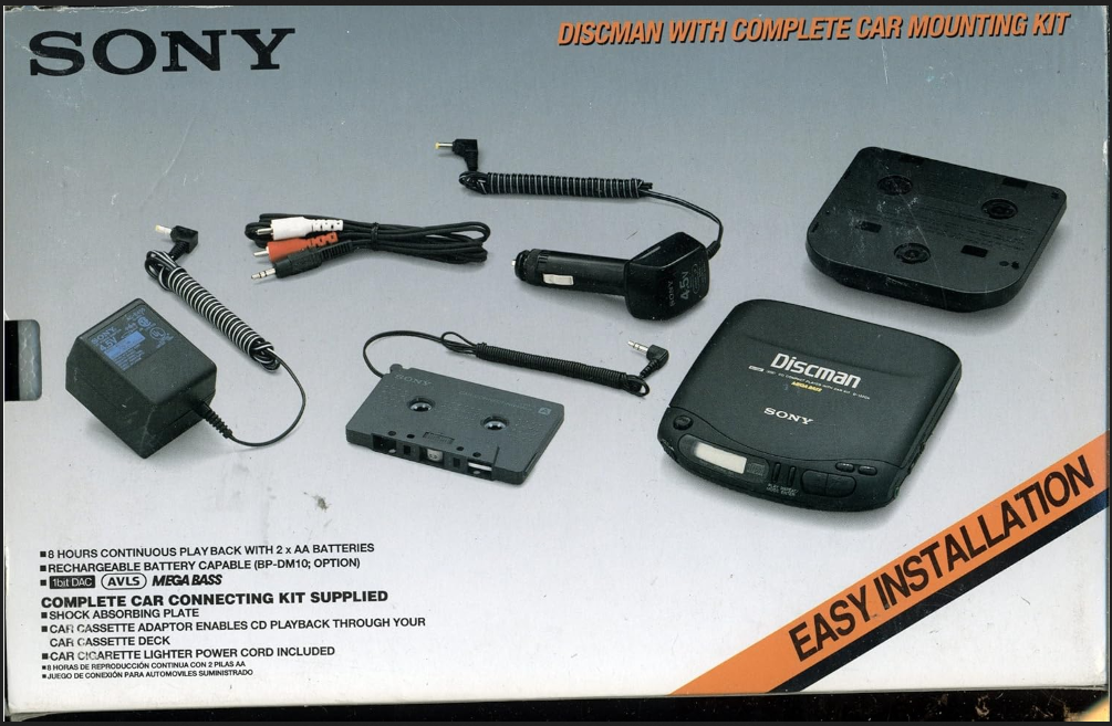 photo of a cardboard box packaging for SONY DISCMAN WITH COMPLETE CAR MOUNTING KIT
package has this text on top of a photo of the discman and accessories listed:
8 HOURS CONTINUOUS PLAY BACK WITH 2 x AA BATTERIES
RECHARGEABLE BATTERY CAPABLE (BP-DM10; OPTION)
1bit DAC AVLS MEGABASS
COMPLETE CAR CONNECTING KIT SUPPLIED
SHOCK ABSORBING PLATE
CAR CASSETTE ADAPTOR ENABLES CD PLAYBACK THROUGH YOUR
CAR CASSETTE DECK
CAR CIGARETTE LIGHTER POWER CORD INCLUDED
beneath the English-language text is this smaller text in Spanish:
8 HORAS DE REPRODUCCIÓN CONTINUA CON 2 PILAS AA
JUEGO DE CONEXIÓN PARA AUTOMOVILES SUMINISTRADO
across the bottom right corner it says:
EASY INSTALLATION